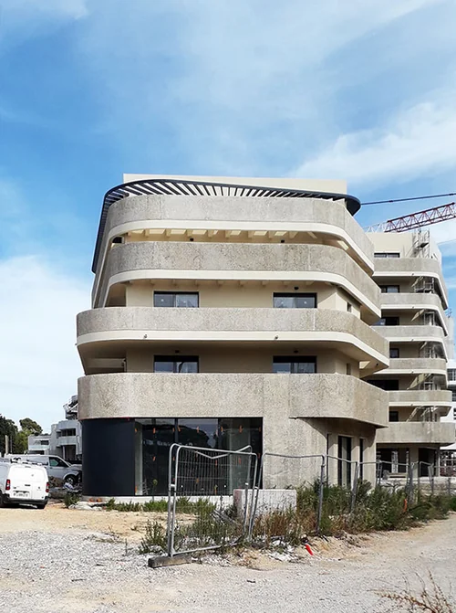 Façade de la résidence accueil de Lattes : balcons arrondis en béton, vitrine au rez-de-chaussée, grue et barrières de chantier encore en place